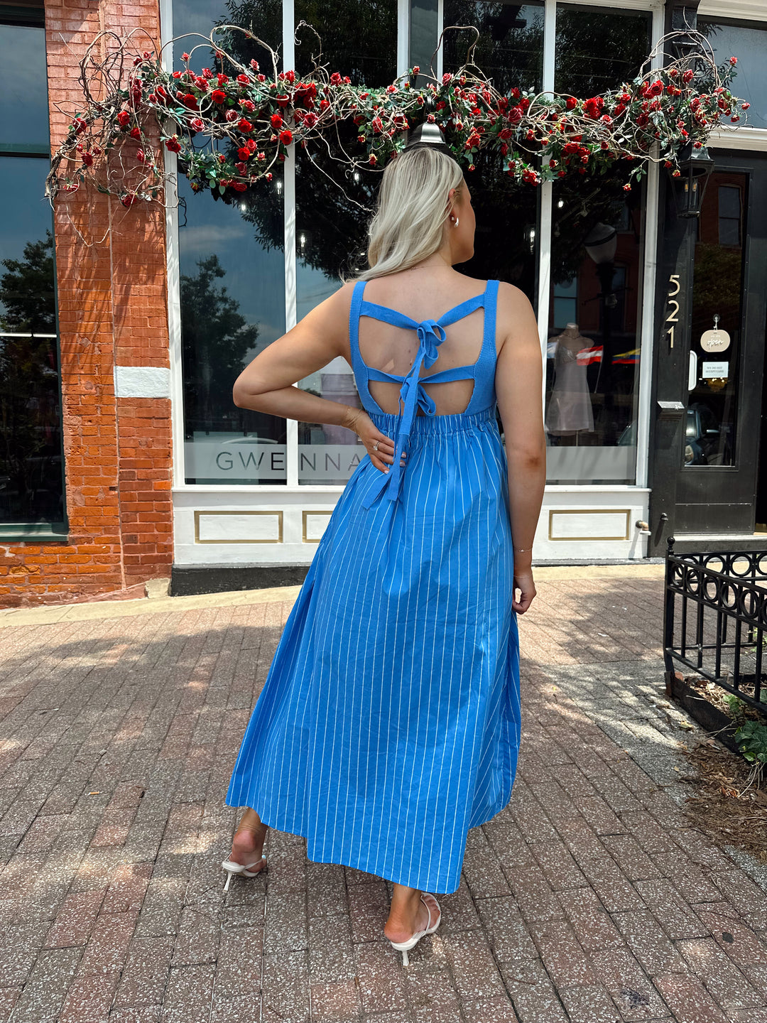 Woman wearing blue striped midi dress with knit bodice, and tie back detail. Has Functional pockets.