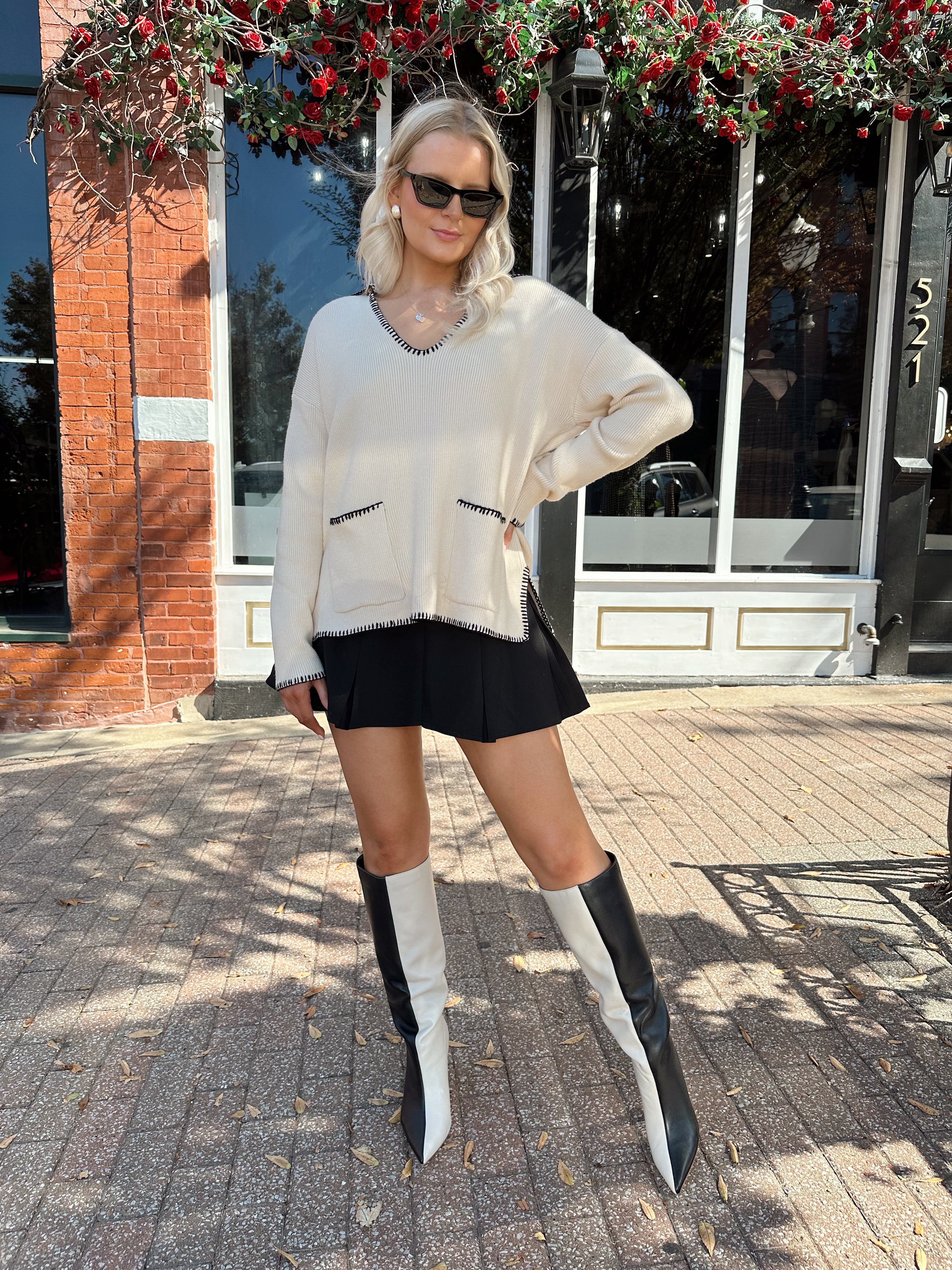 Woman wearing oatmeal sweater with black stitching and front pockets.
