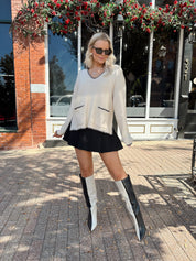 Woman wearing oatmeal sweater with black stitching and front pockets.