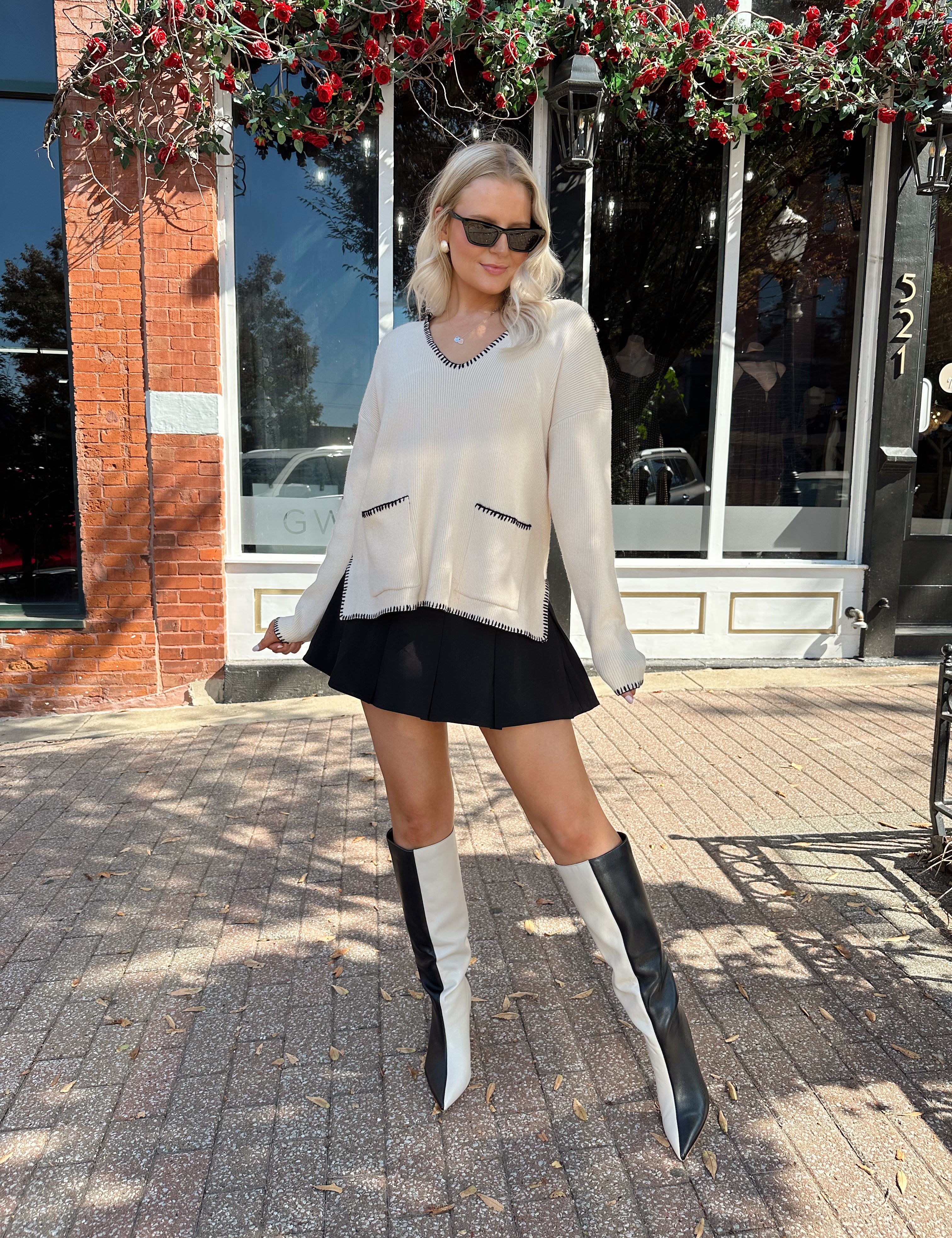 Woman wearing oatmeal sweater with black stitching and front pockets.
