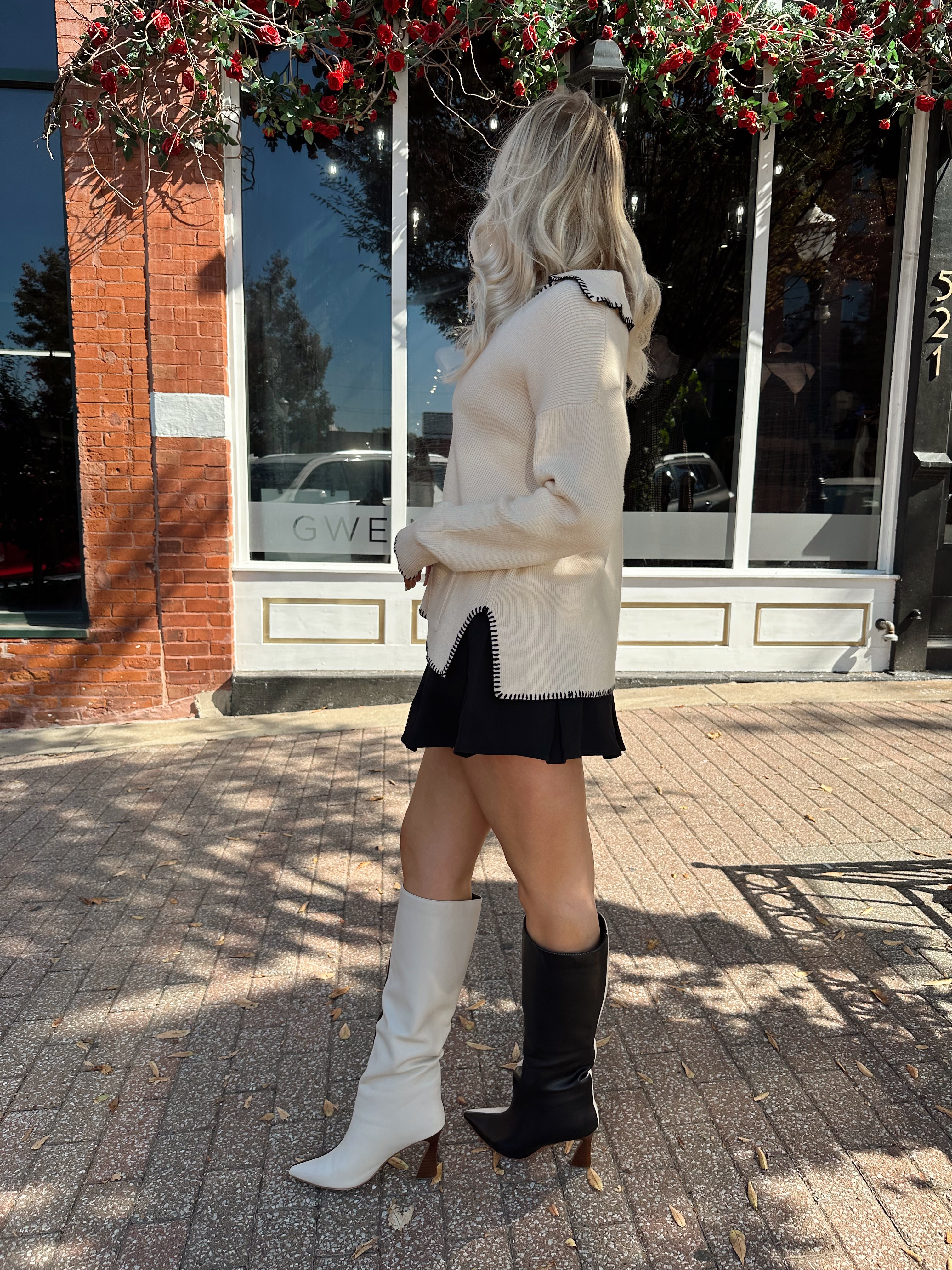 Woman wearing oatmeal sweater with black stitching and front pockets.