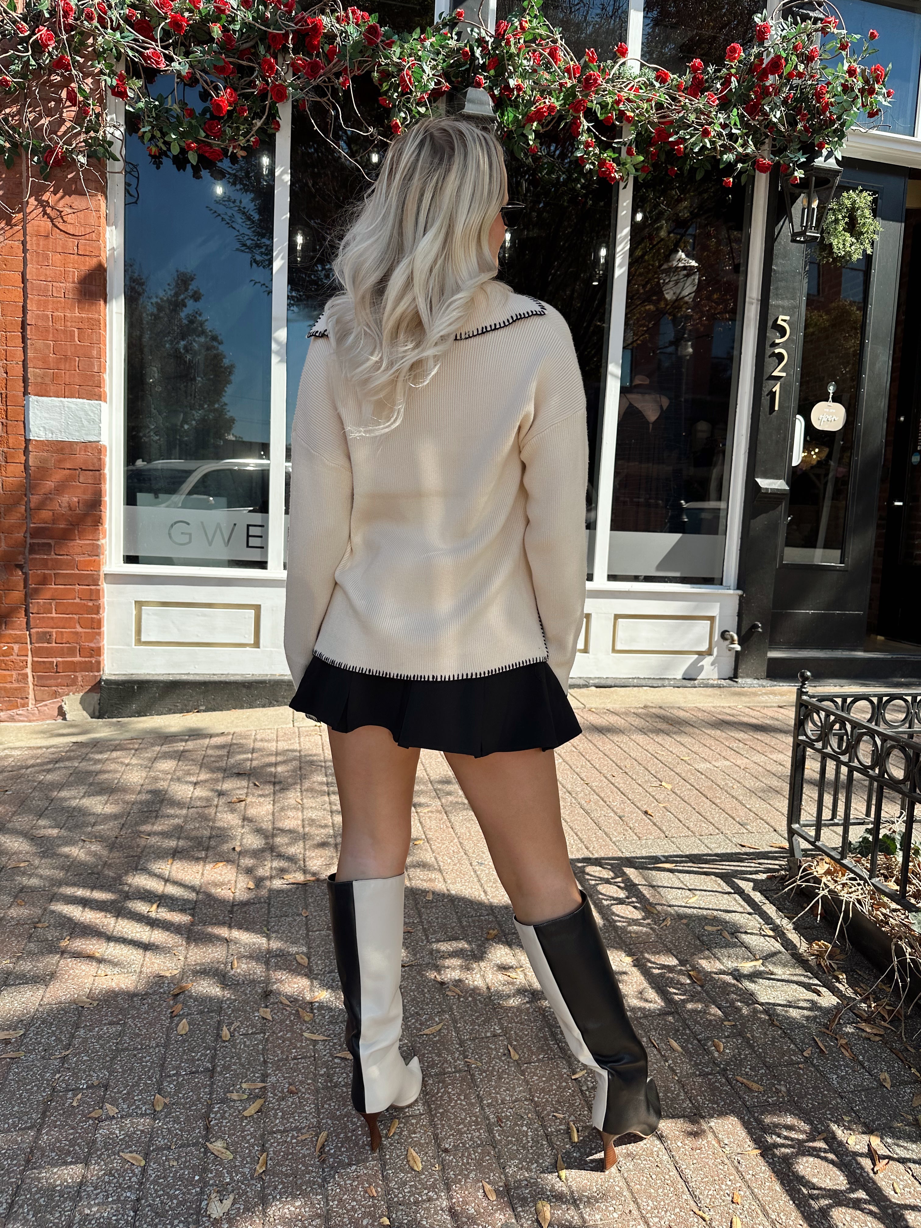 Woman wearing oatmeal sweater with black stitching and front pockets.