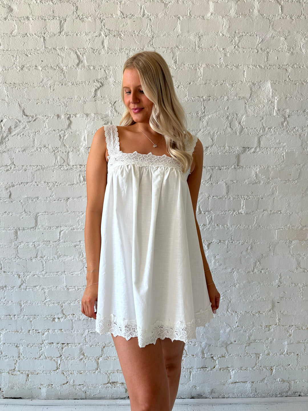 Woman wearing white shift style mini dress with lave trim detail and straps. 