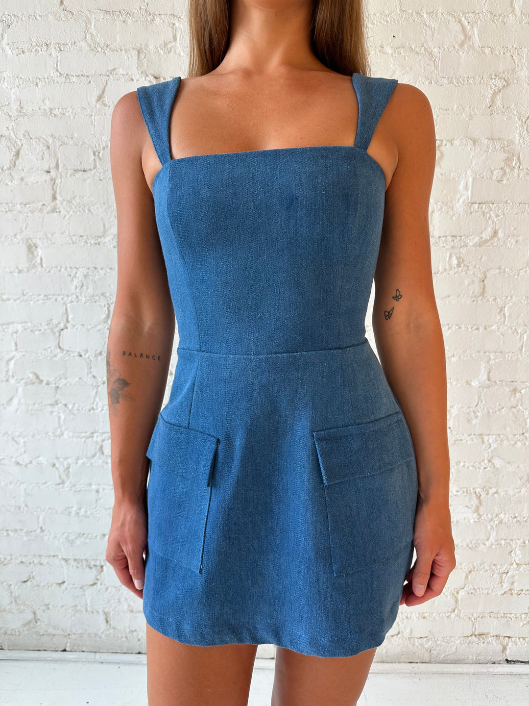 Woman wearing dark wash denim mini dress with square neckline, and built in shorts. 
