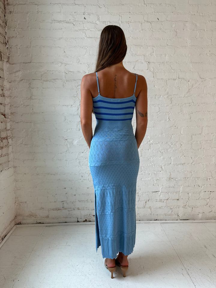 Woman wearing blue knit maxi dress with contrast blue lining, and side slit.