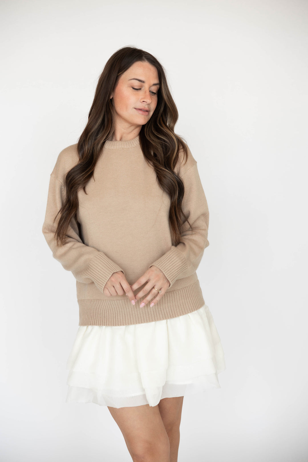 Woman wearing beige sweater mini dress with a cream tiered skirt. 