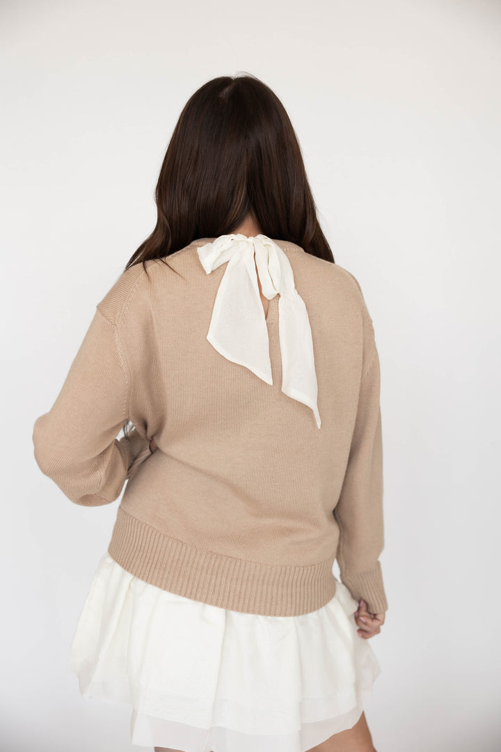 Woman wearing beige sweater mini dress with a cream tiered skirt. 