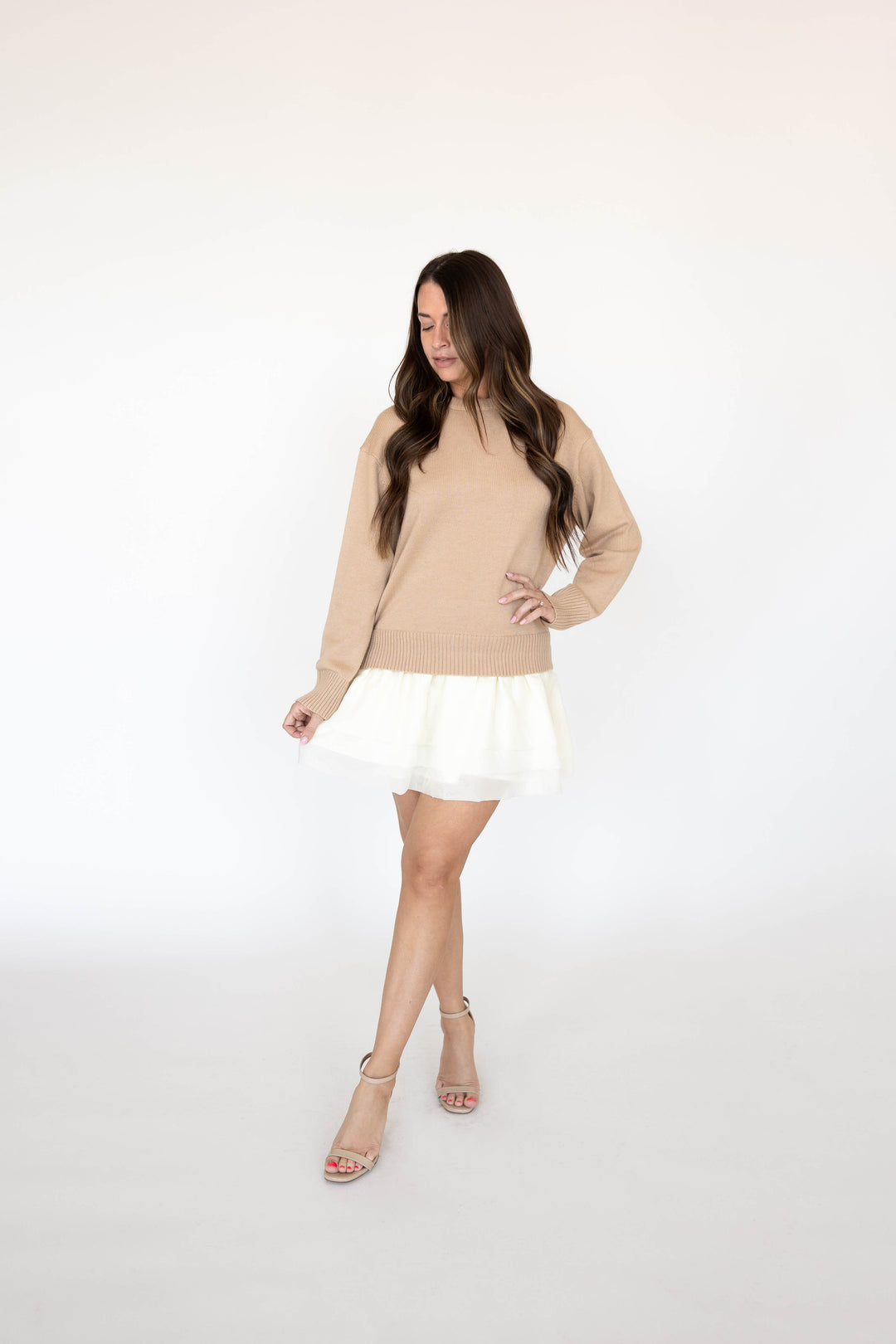 Woman wearing beige sweater mini dress with a cream tiered skirt. 