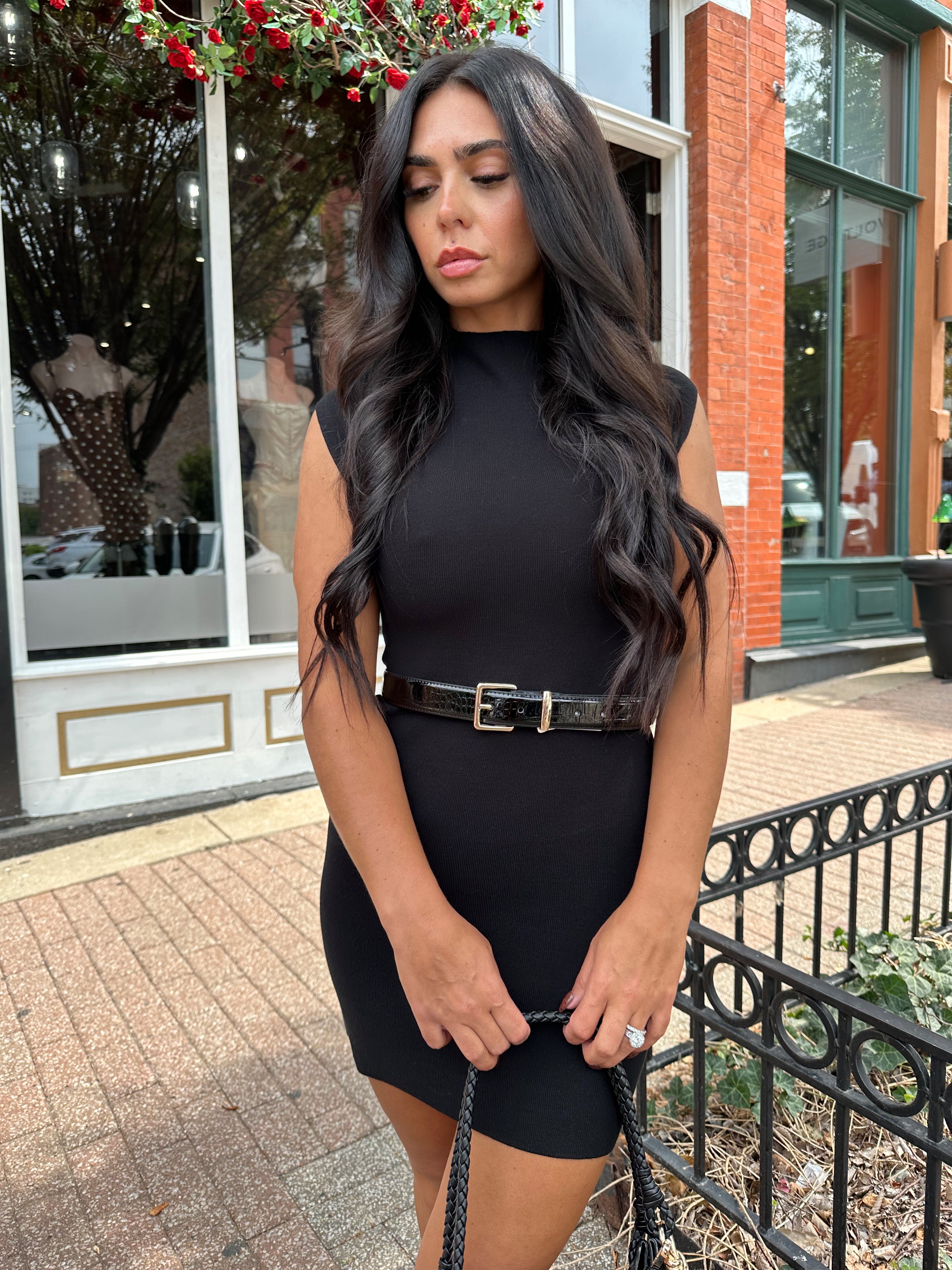 Woman wearing a black ribbed mock neck mini dress with belt.