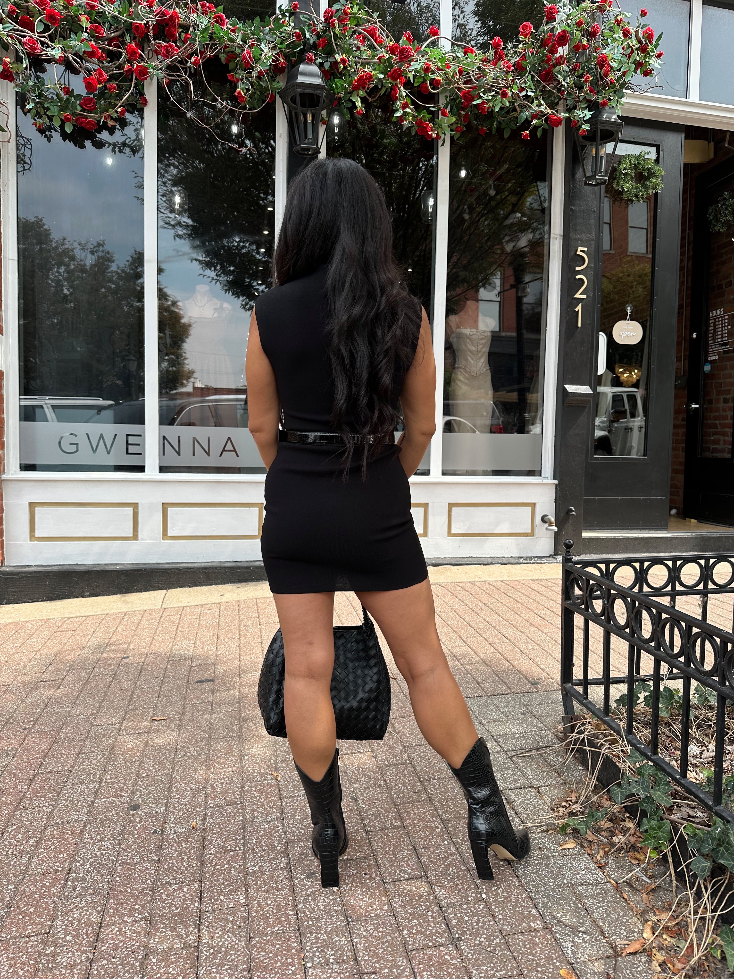 Woman wearing a black ribbed mock neck mini dress with belt.