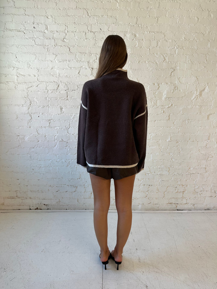 Woman wearing boxy brown oversized sweater with contrast trim and brown leather short. 