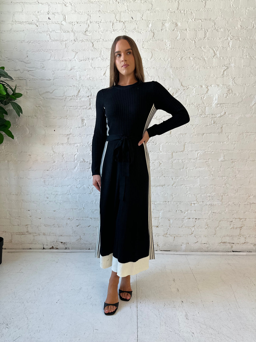 Woman wearing black long sleeve maxi dress with white contrast lining and belted midsection. 