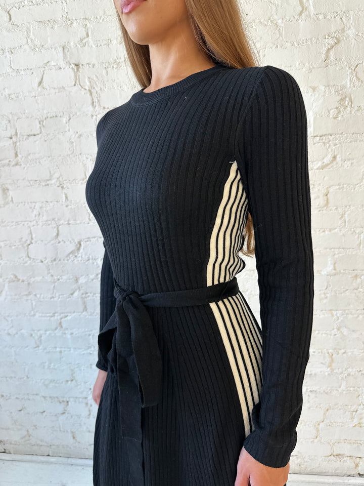 Woman wearing black long sleeve maxi dress with white contrast lining and belted midsection. 