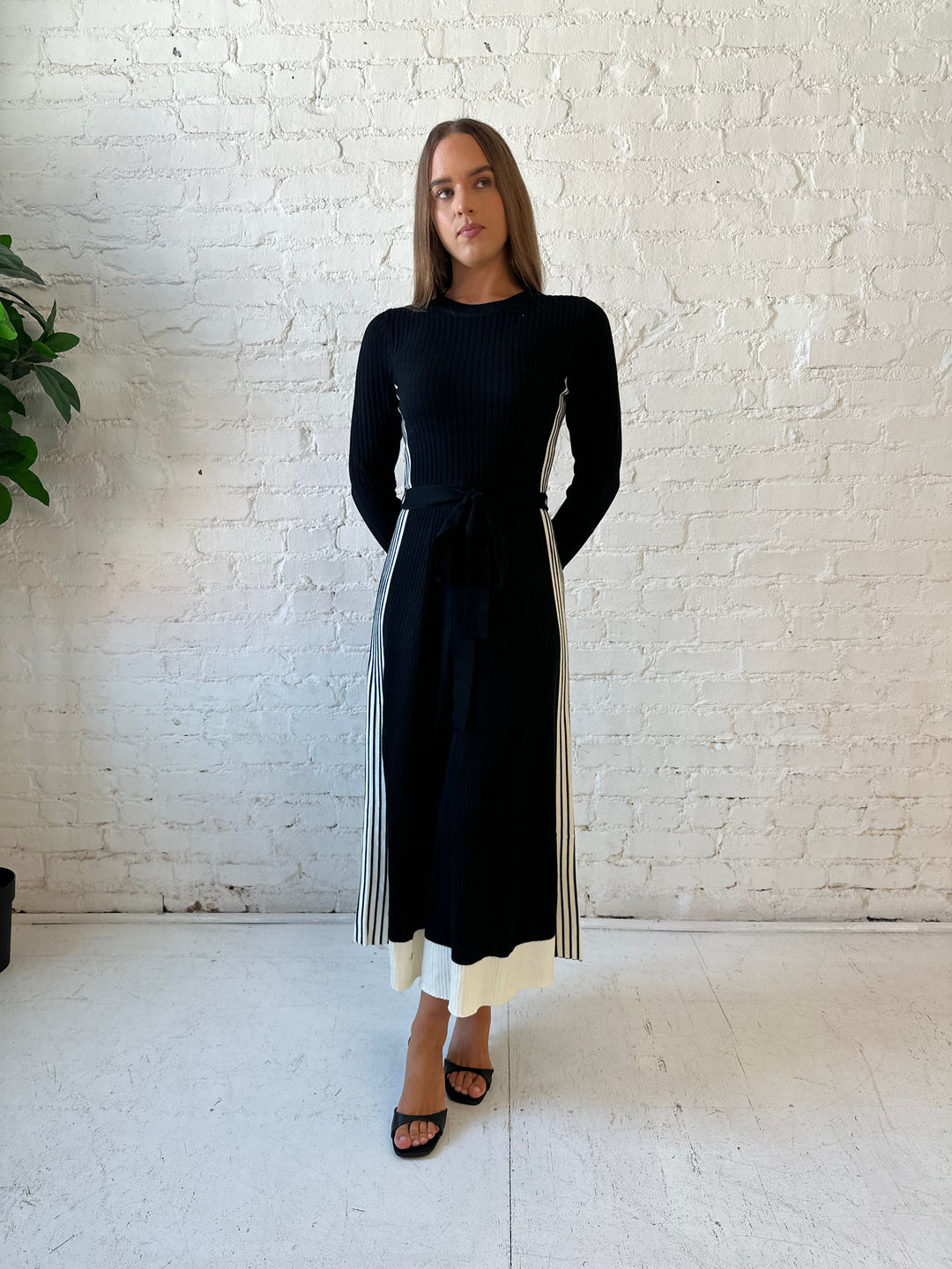 Woman wearing black long sleeve maxi dress with white contrast lining and belted midsection. 