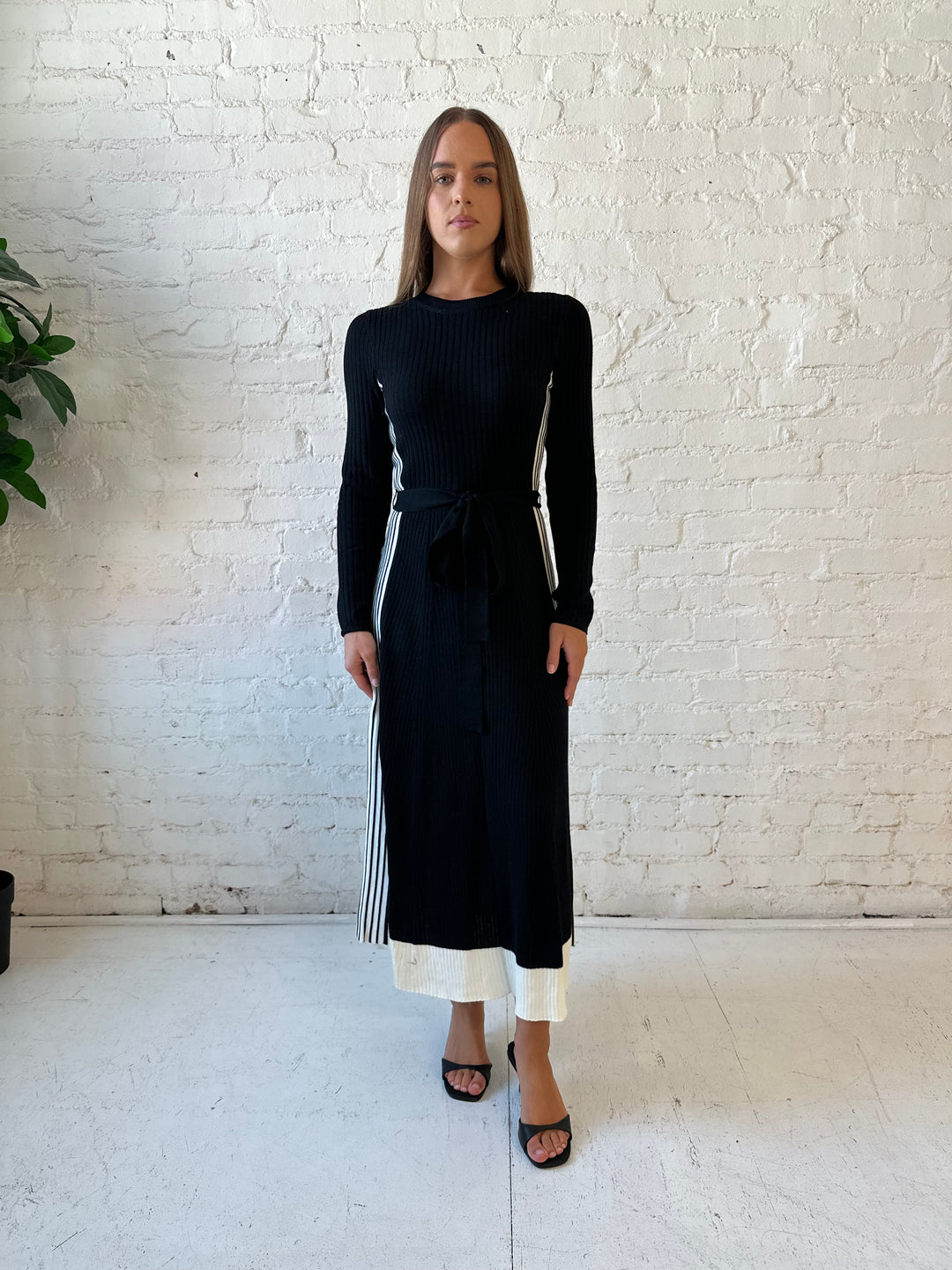 Woman wearing black long sleeve maxi dress with white contrast lining and belted midsection. 