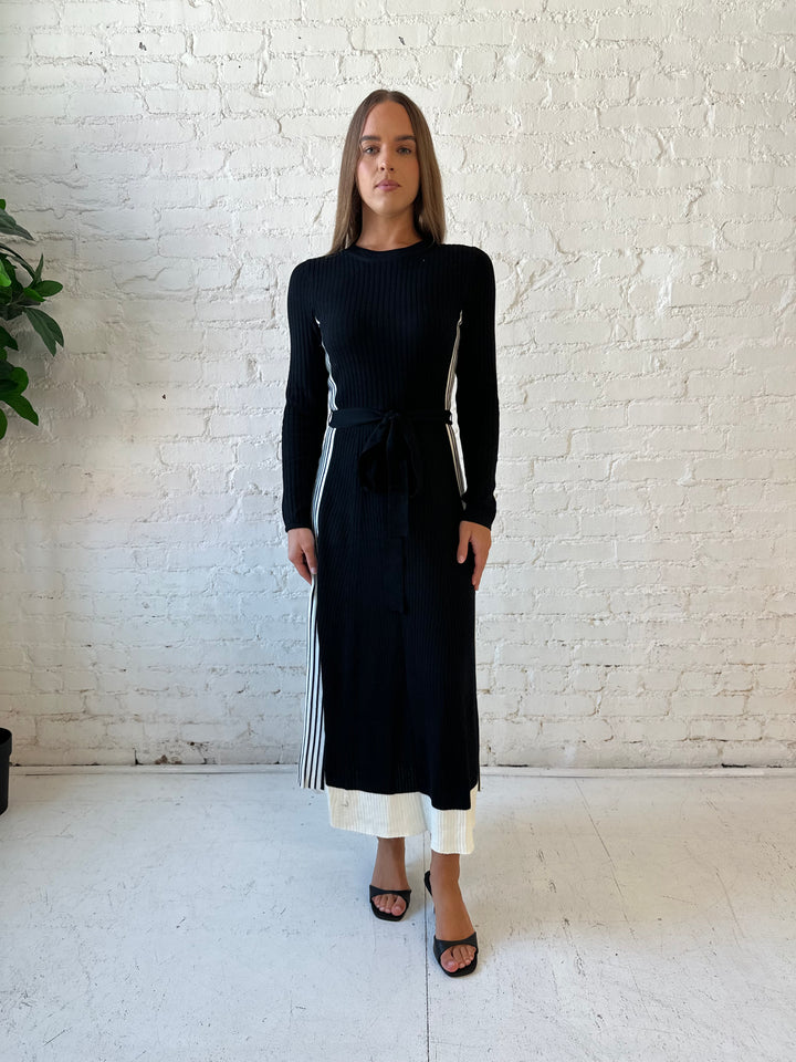 Woman wearing black long sleeve maxi dress with white contrast lining and belted midsection. 