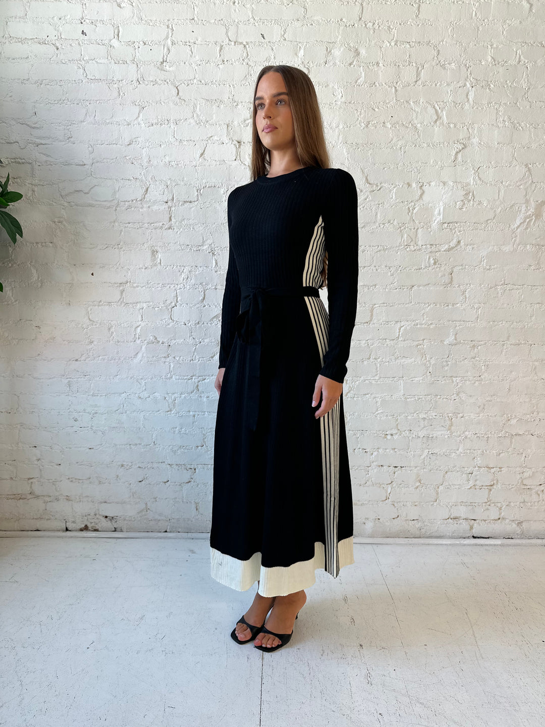 Woman wearing black long sleeve maxi dress with white contrast lining and belted midsection. 