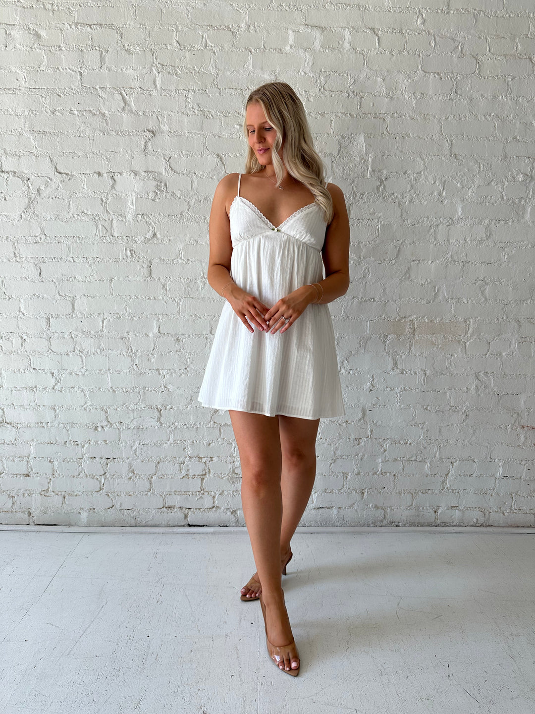 Woman wearing white mini dress with eyelet detailing. 