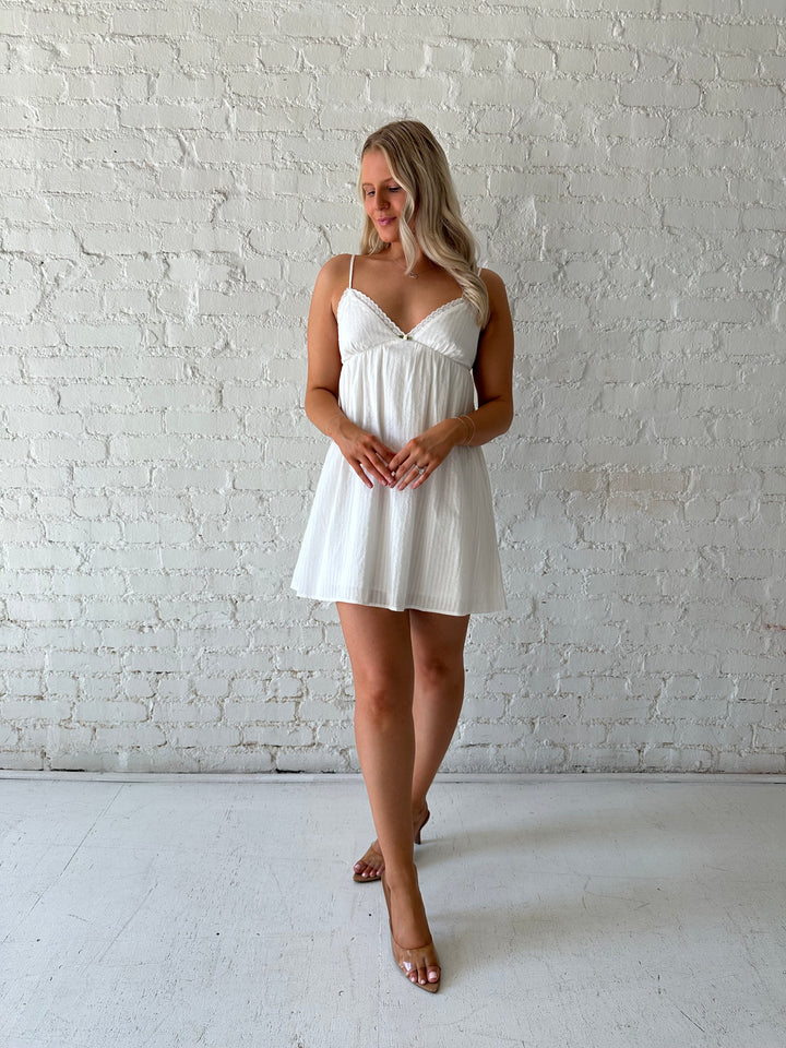 Woman wearing white mini dress with eyelet detailing. 