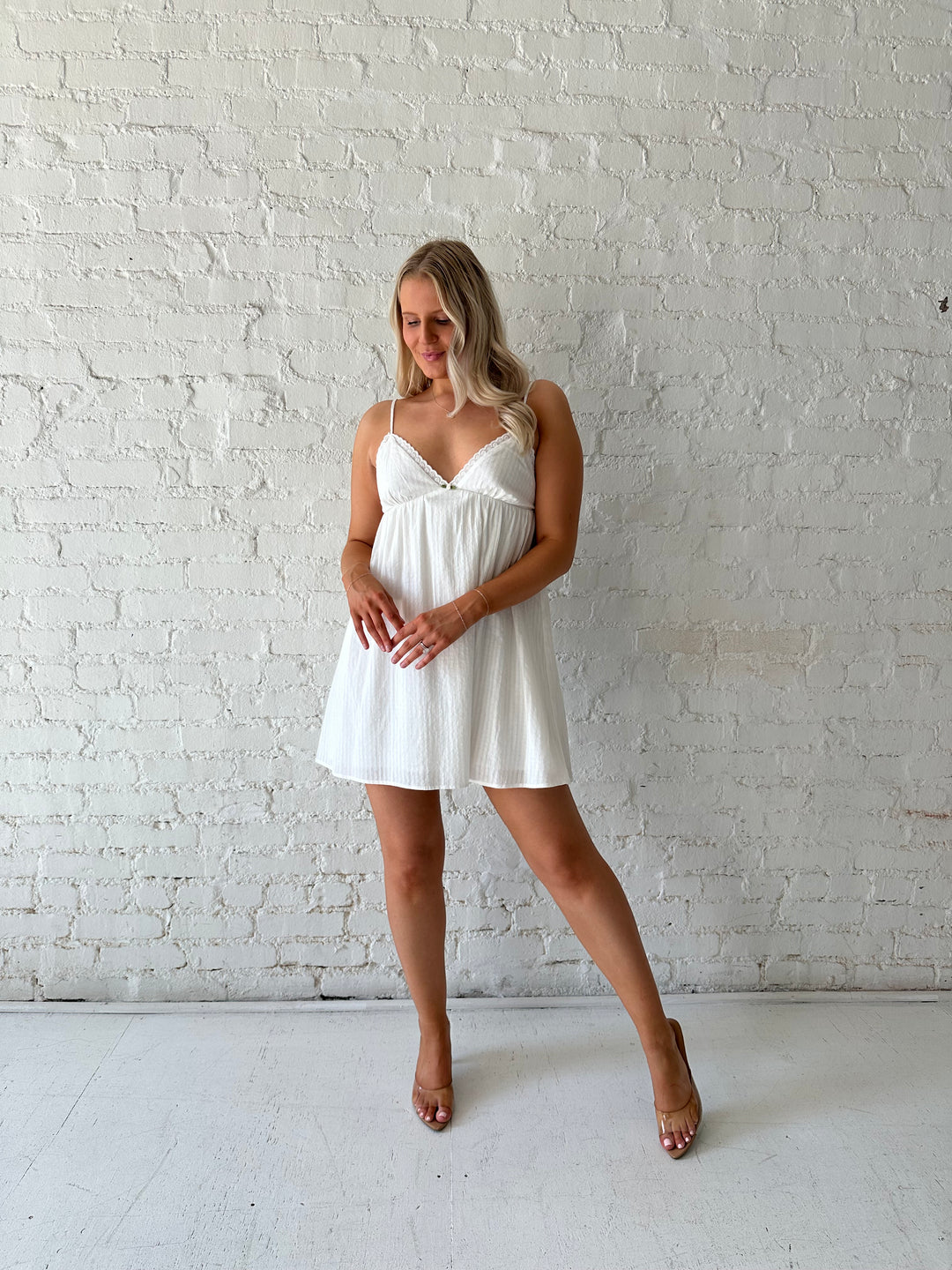 Woman wearing white mini dress with eyelet detailing. 