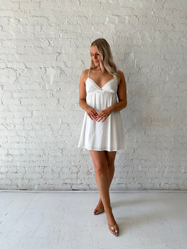 Woman wearing white mini dress with eyelet detailing. 