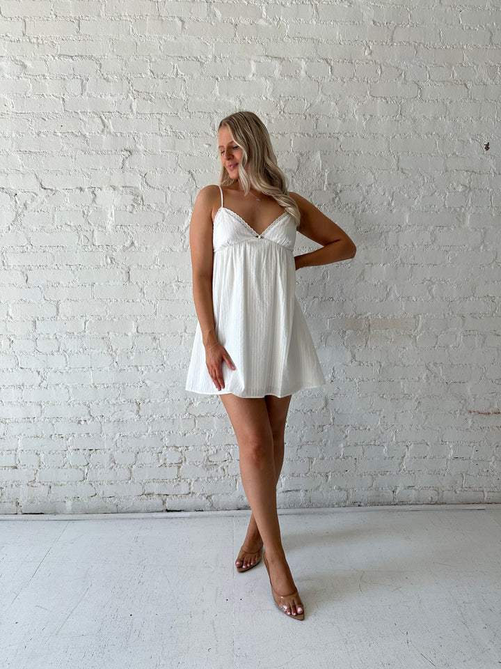 Woman wearing white mini dress with eyelet detailing. 