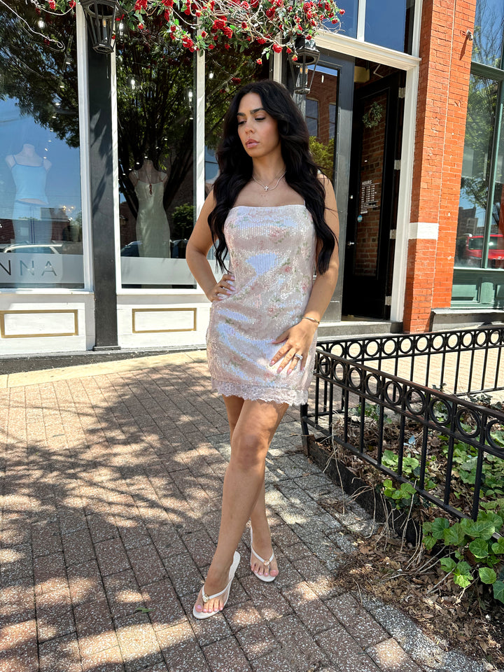 Woman wearing wearing blush pink sequin mini dress with rose pattern, and lace trim.