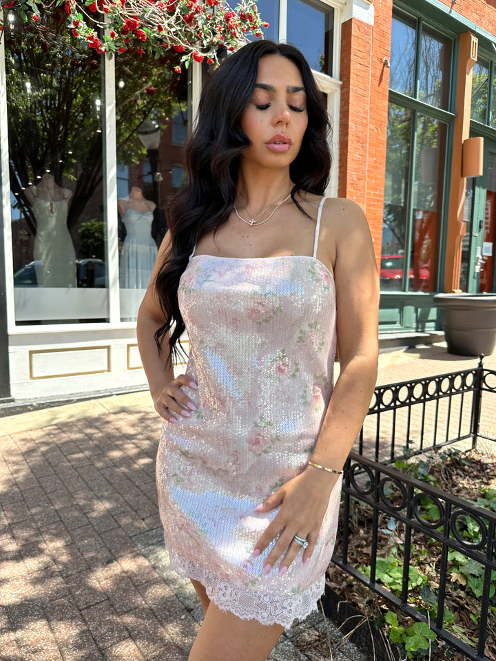 Woman wearing wearing blush pink sequin mini dress with rose pattern, and lace trim.