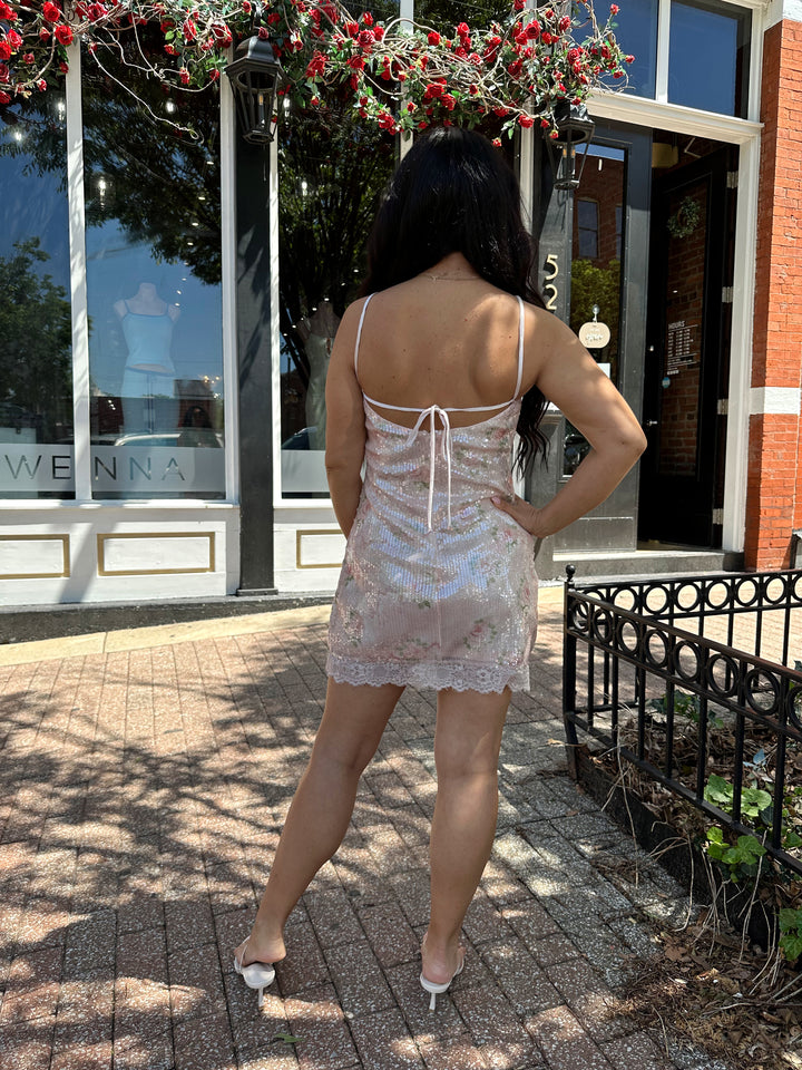 Woman wearing wearing blush pink sequin mini dress with rose pattern, and lace trim.