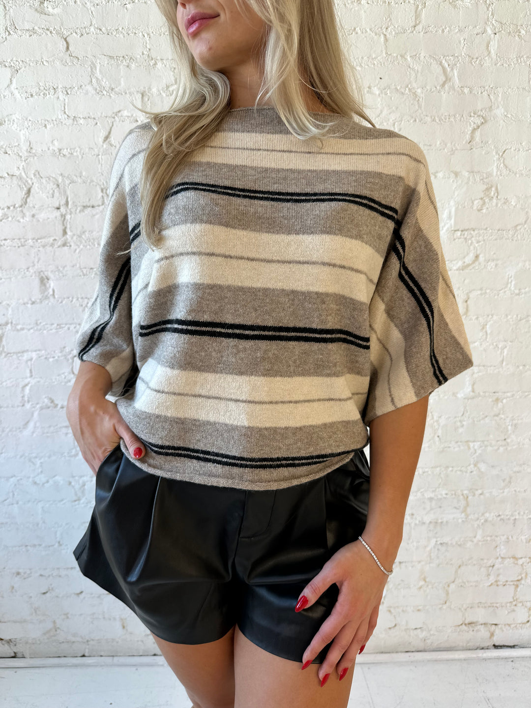 Woman wearing neutral striped slouchy off the shoulder short sleeve top with black faux leather shorts. 