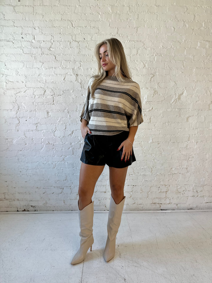 Woman wearing neutral striped slouchy off the shoulder short sleeve top with black faux leather shorts. 