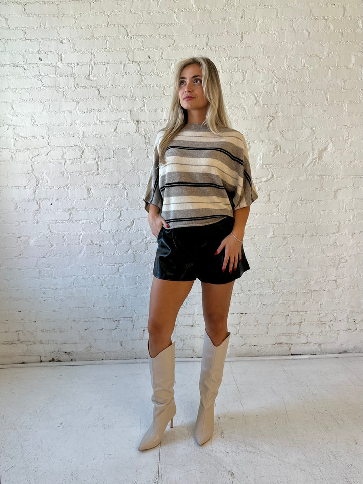 Woman wearing neutral striped slouchy off the shoulder short sleeve top with black faux leather shorts. 