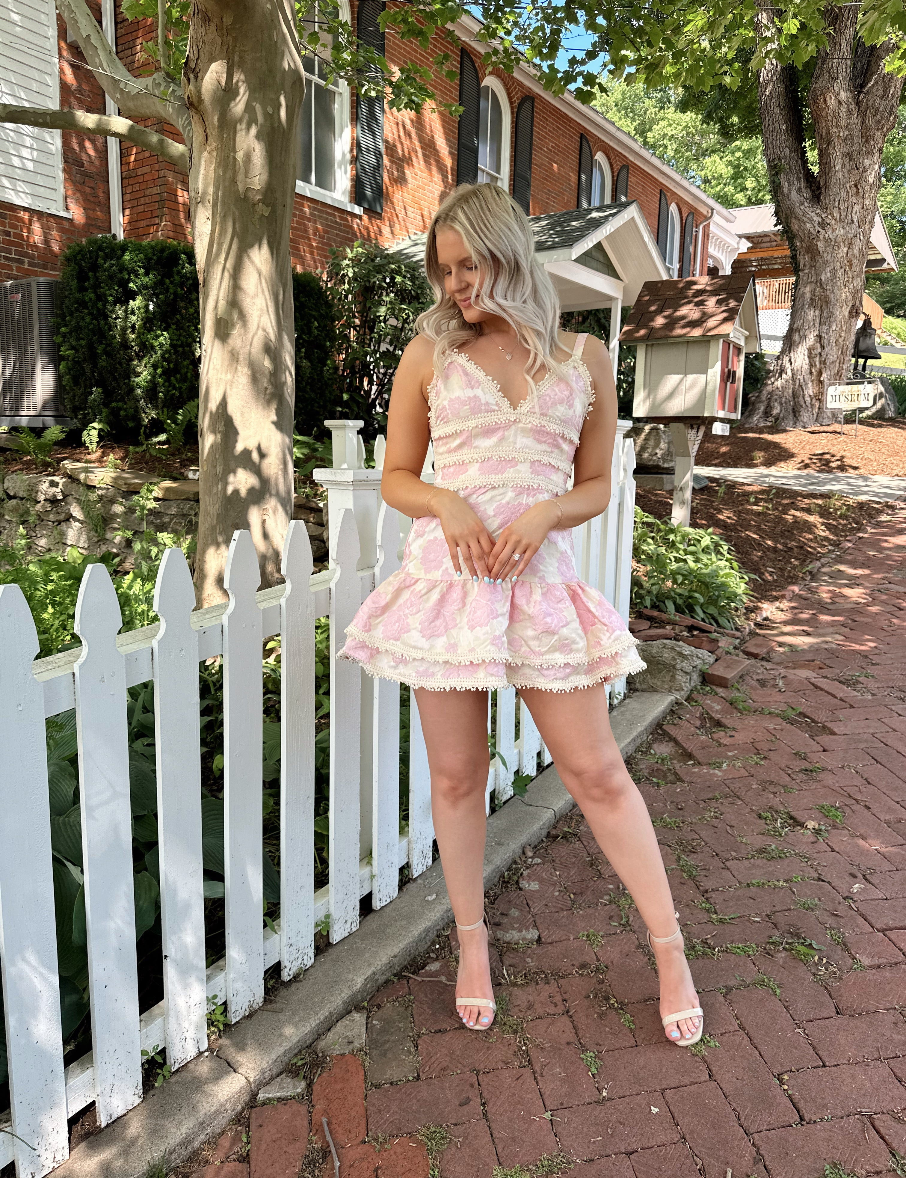 Woman in a pink textured floral mini dress with pearl trim and a flouncy ruffle hem