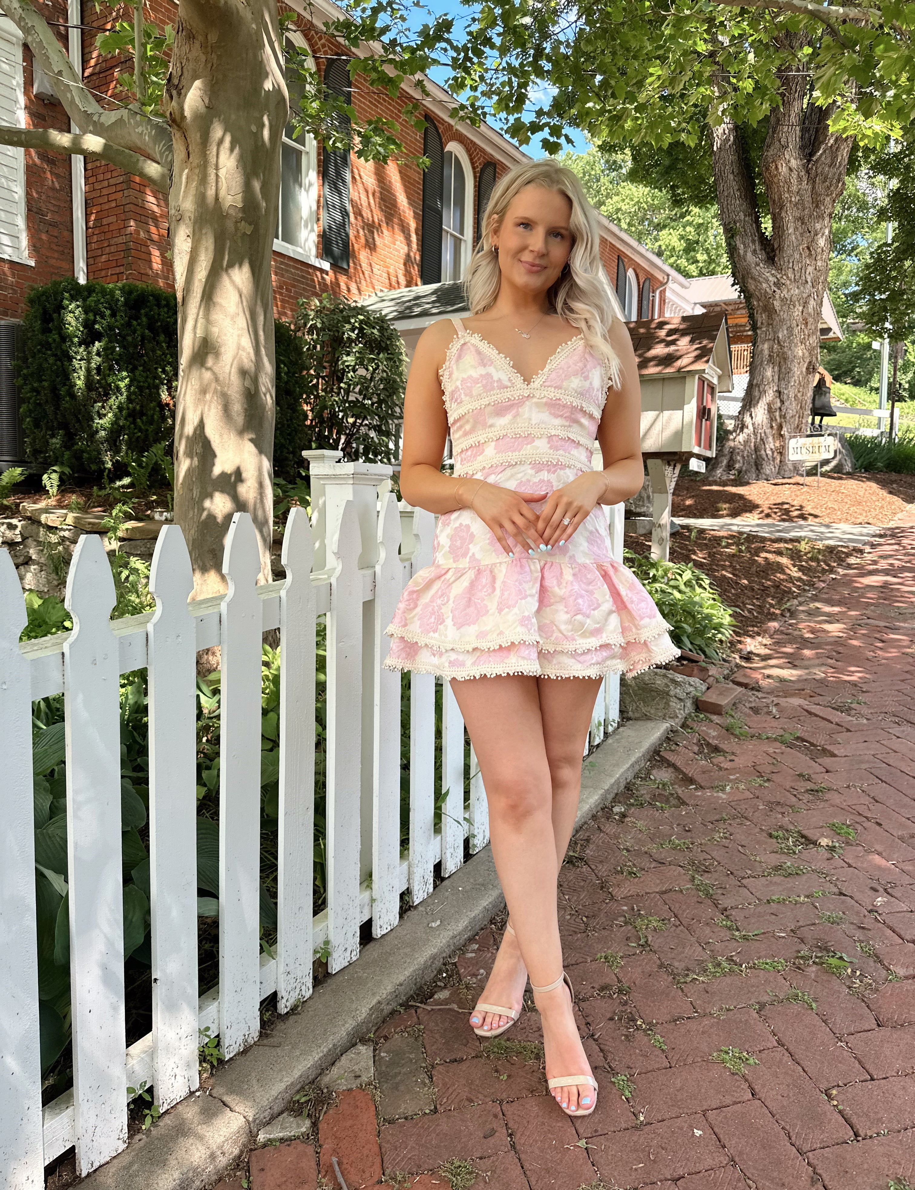 Woman in a pink textured floral mini dress with pearl trim and a flouncy ruffle hem