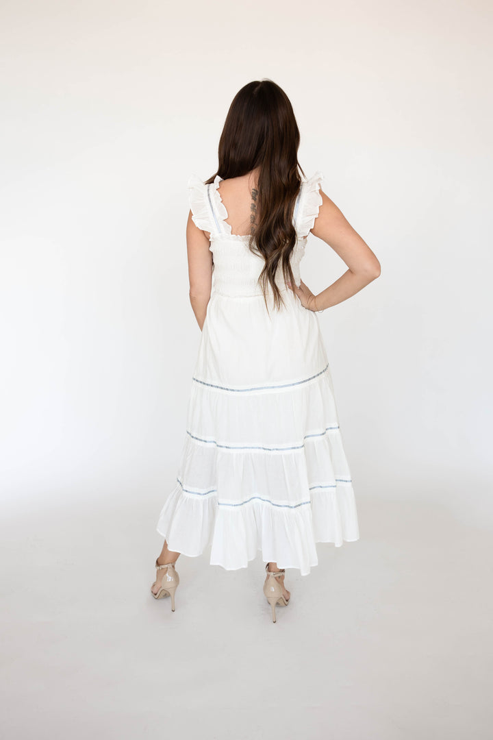 Woman wearing white smocked tiered midi dress with blue ribbon detailing. 