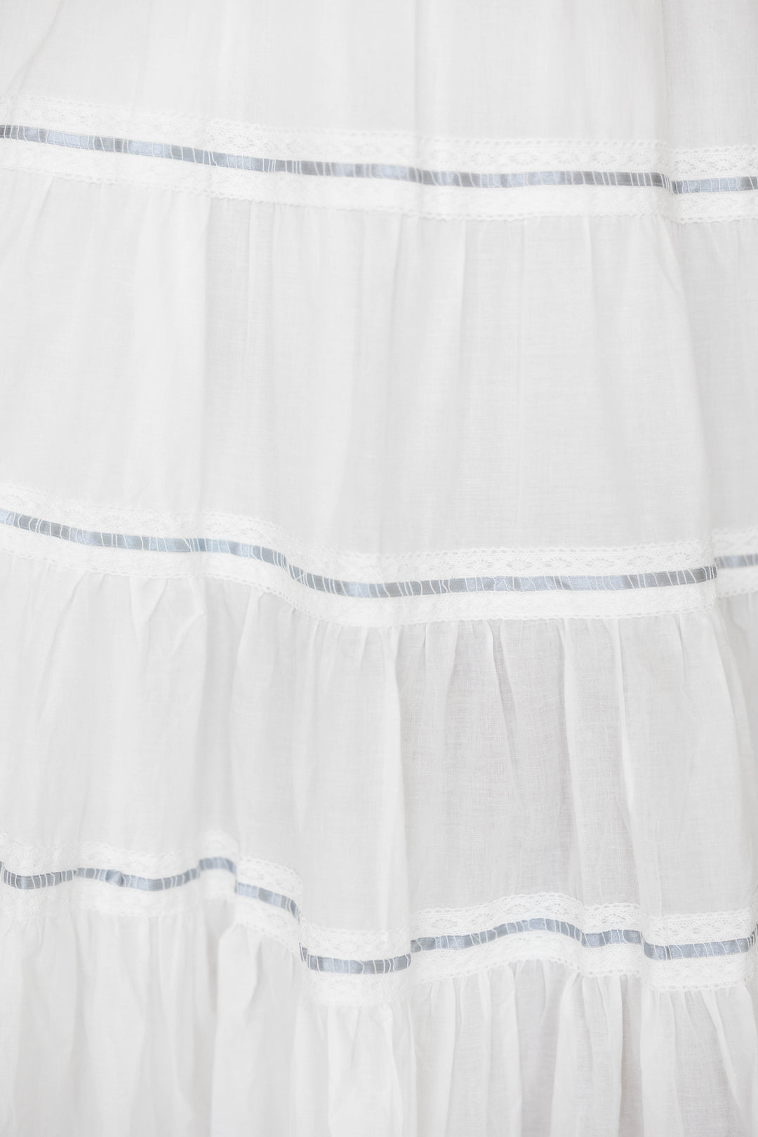 Woman wearing white smocked tiered midi dress with blue ribbon detailing. 