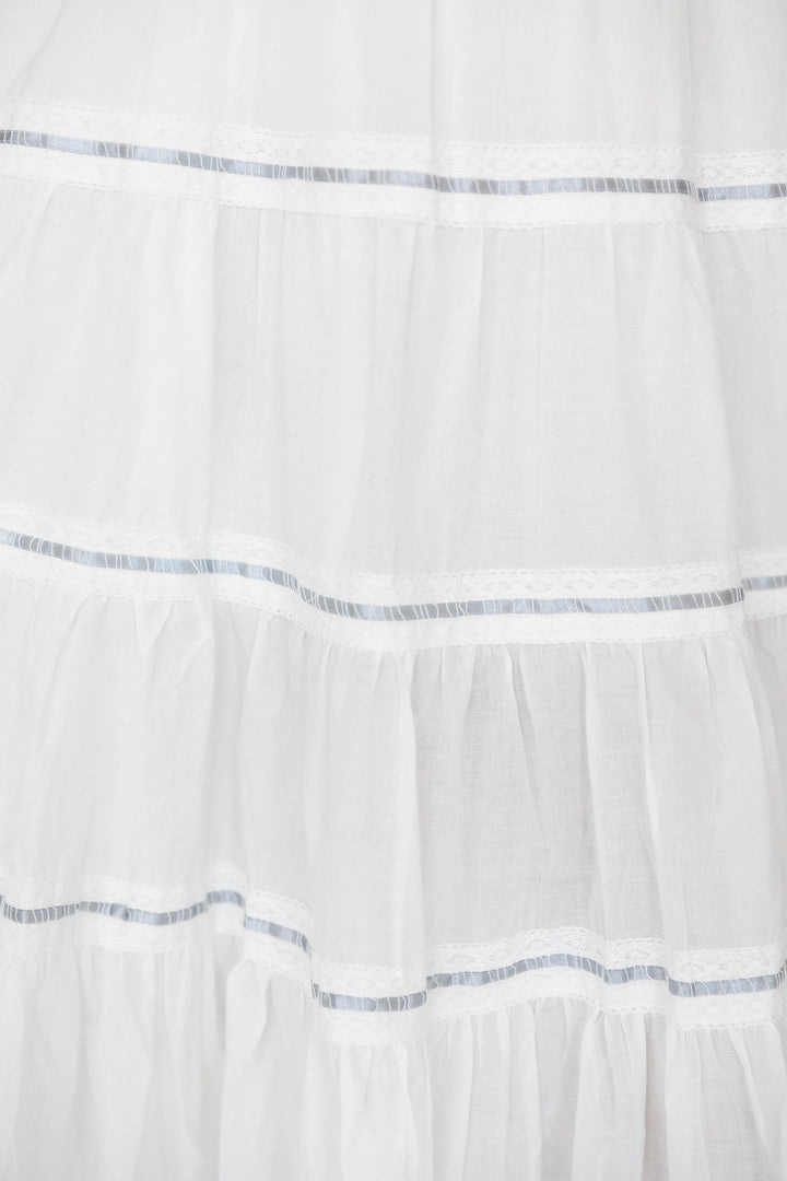 Woman wearing white smocked tiered midi dress with blue ribbon detailing. 