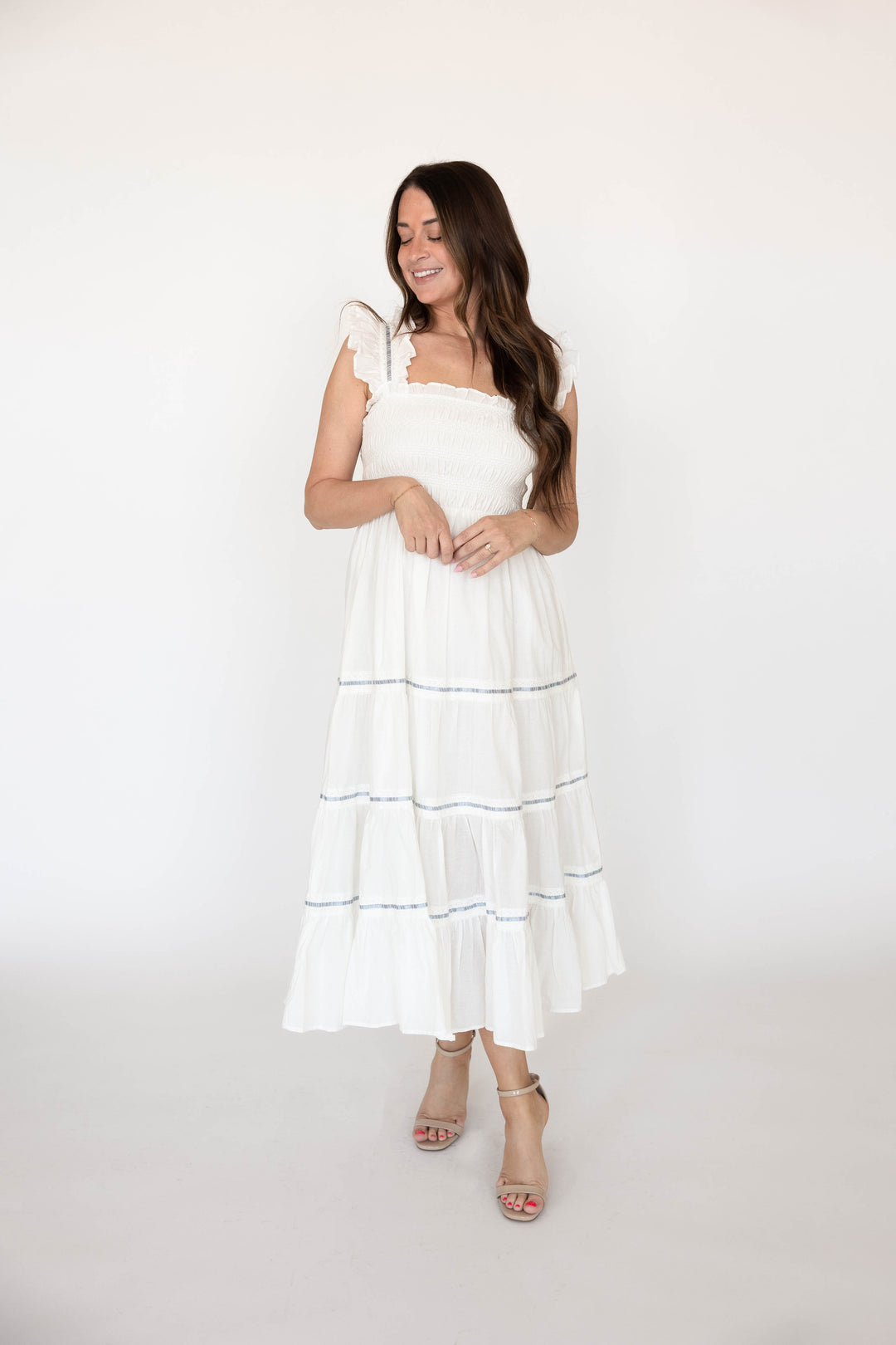 Woman wearing white smocked tiered midi dress with blue ribbon detailing. 