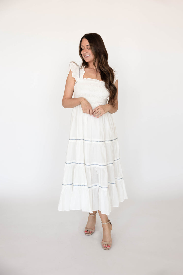 Woman wearing white smocked tiered midi dress with blue ribbon detailing. 