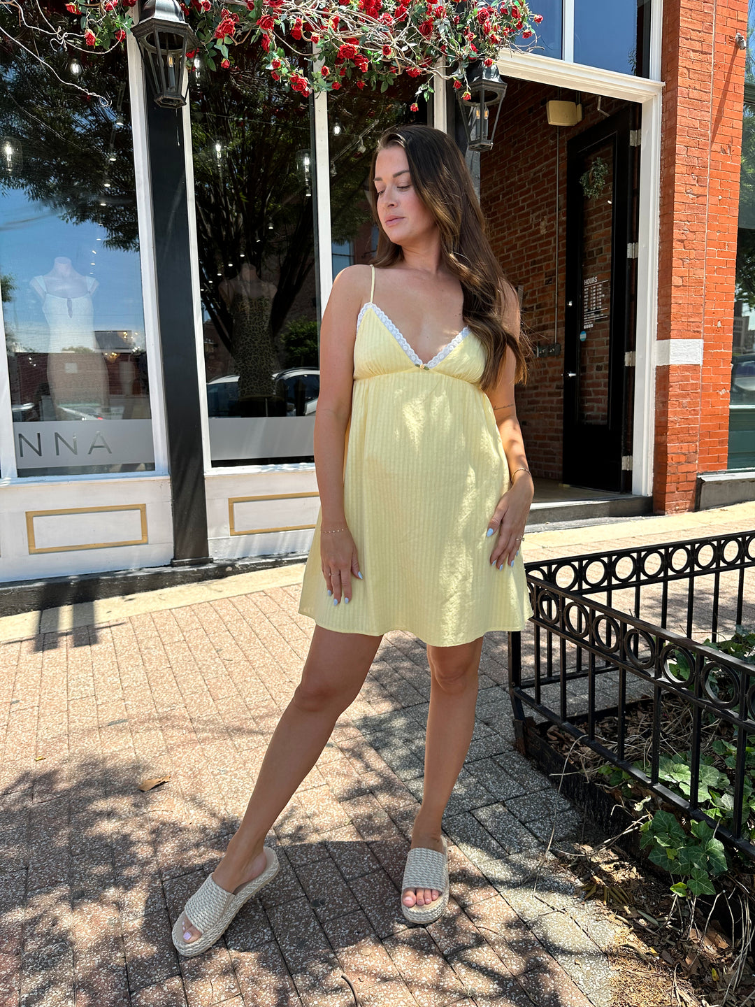 Woman wearing yellow striped mini dress with lace trim neckline, and platform sandals.