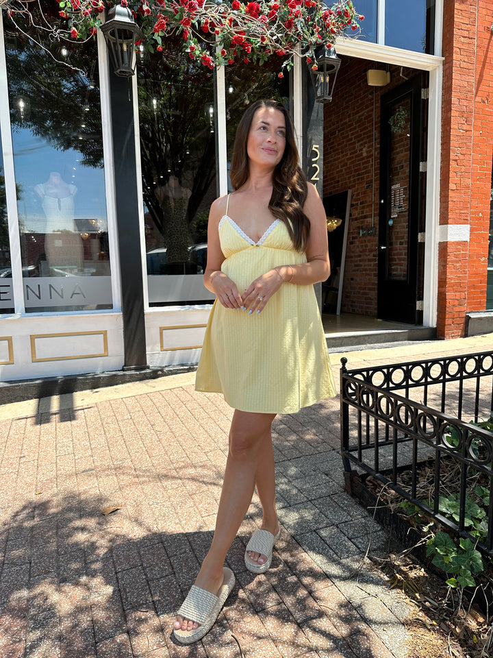 Woman wearing yellow striped mini dress with lace trim neckline, and platform sandals.