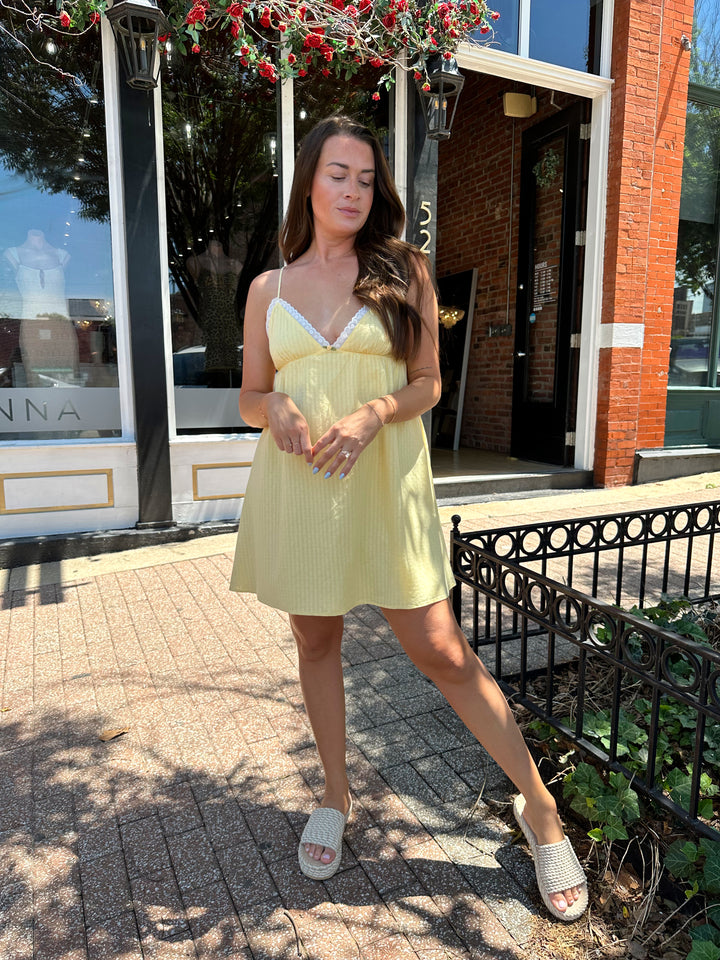 Woman wearing yellow striped mini dress with lace trim neckline, and platform sandals.