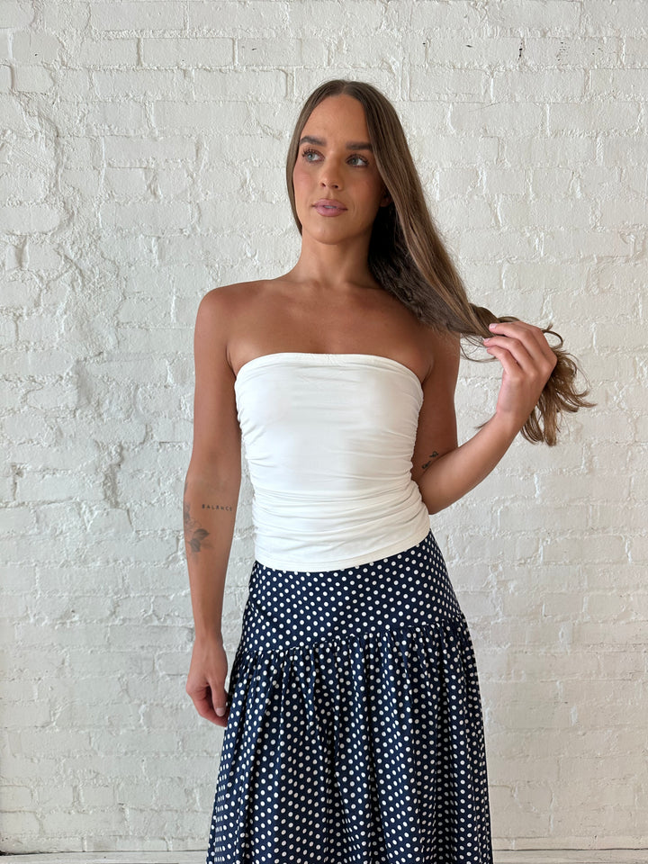 Woman wearing white ruched tube top with navy polka dot maxi skirt.