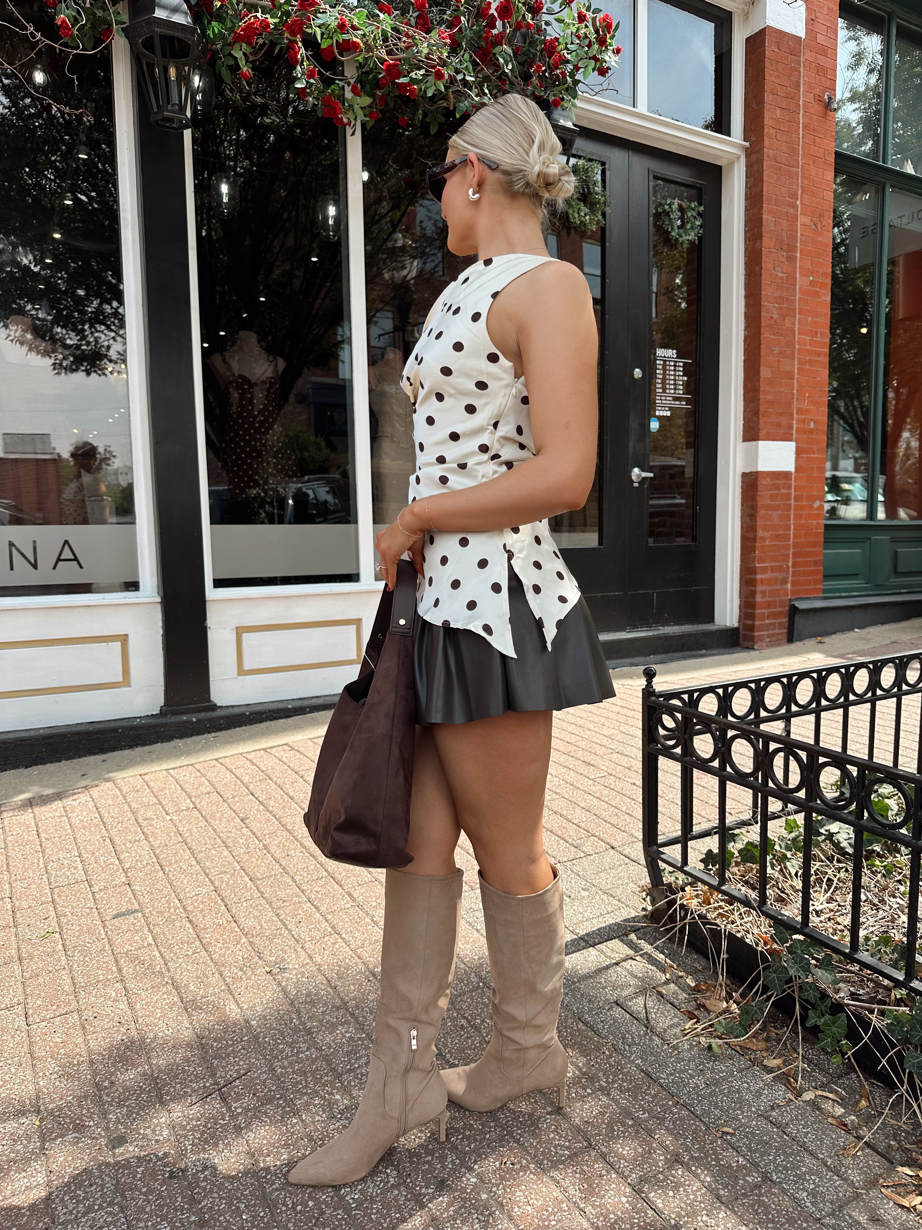 Woman wearing one shoulder satin polka dot top with brown leather pleated mini skirt. 