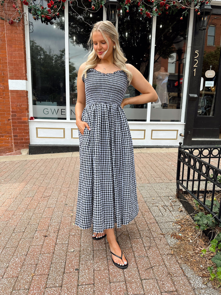 Woman wearing black and white gingham midi dress with smocked bodice and adjustable straps.