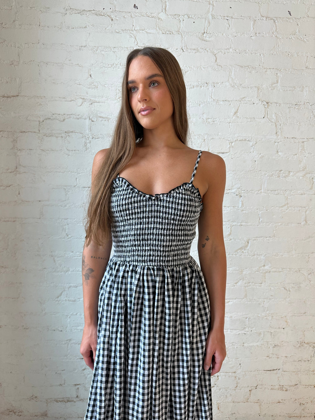Woman wearing black gingham midi dress with smocked bodice.