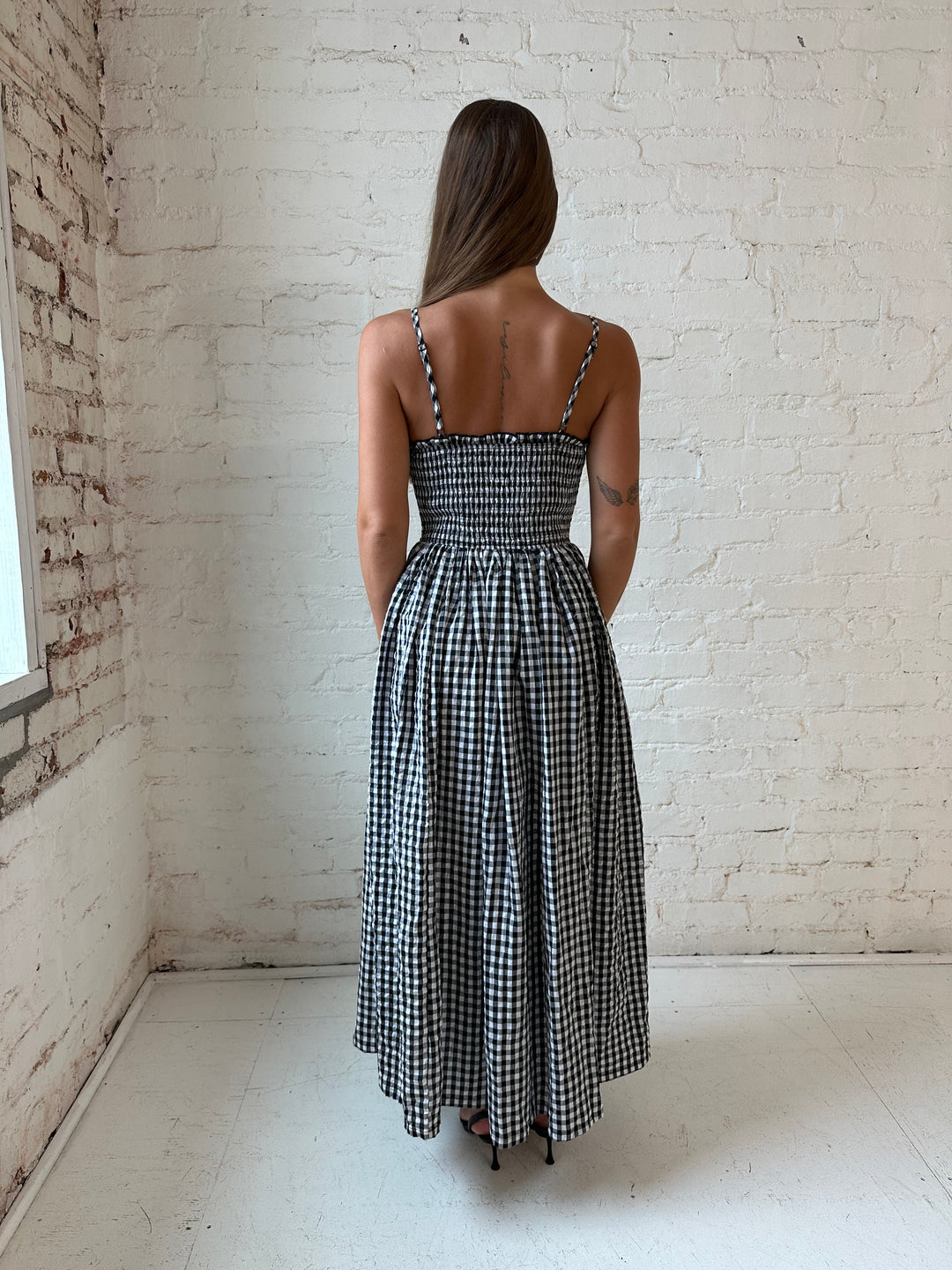 Woman wearing black gingham midi dress with smocked bodice.