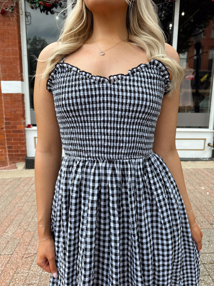 Woman wearing black and white gingham midi dress with smocked bodice and adjustable straps.