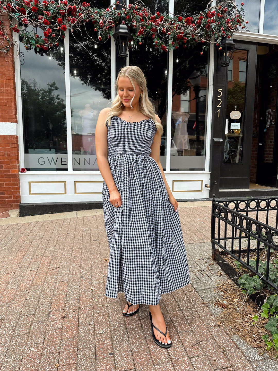 Woman wearing black and white gingham midi dress with smocked bodice and adjustable straps.
