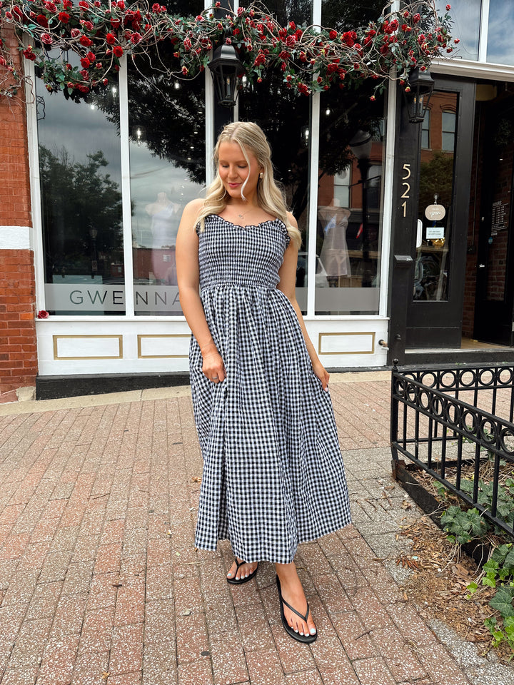 Woman wearing black and white gingham midi dress with smocked bodice and adjustable straps.
